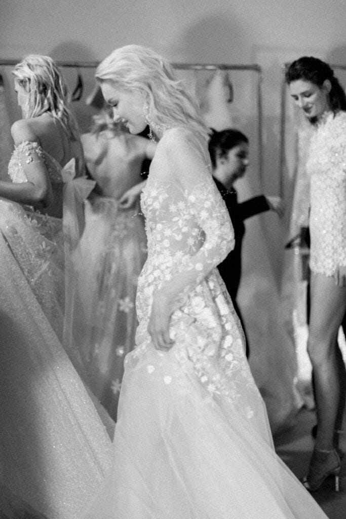 Women in floral gowns backstage at fashion show.