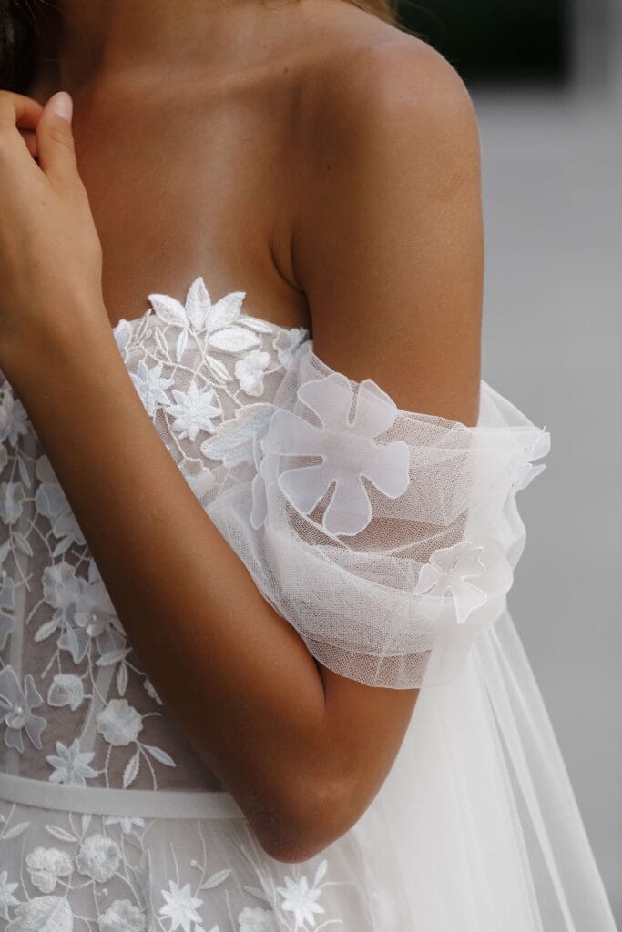 Woman in sheer floral off-shoulder wedding dress.