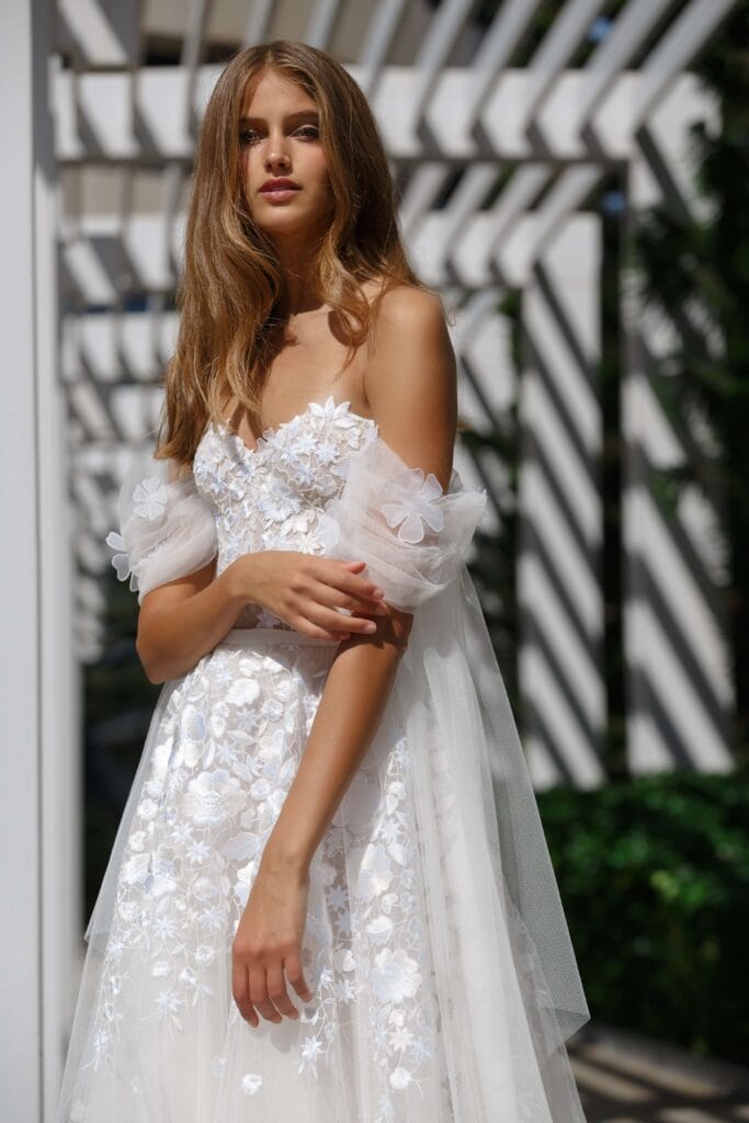 Woman in floral wedding dress by pergola.