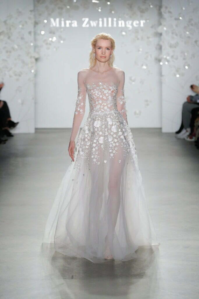 Model in sheer white floral gown on runway.