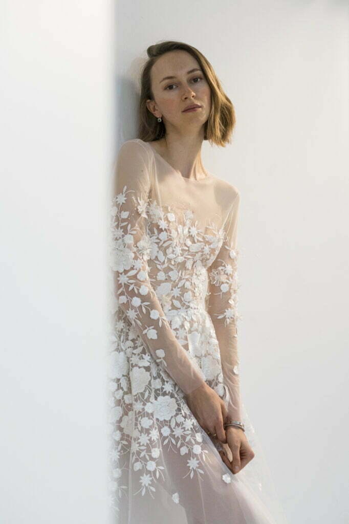 Woman in sheer floral dress against white wall.