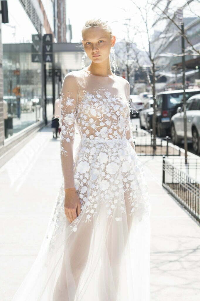 Woman in white lace gown on city sidewalk.
