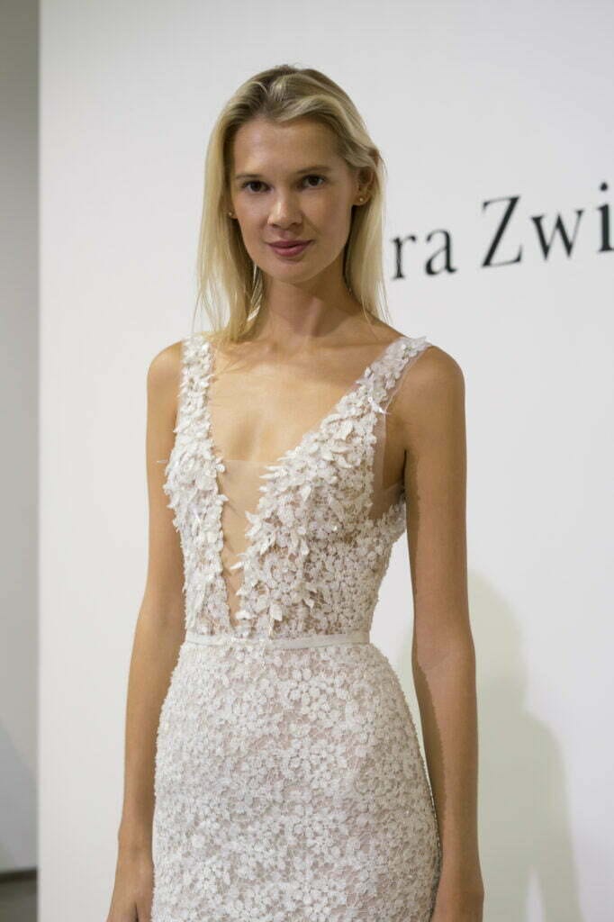 Blonde woman in white lace dress stands.