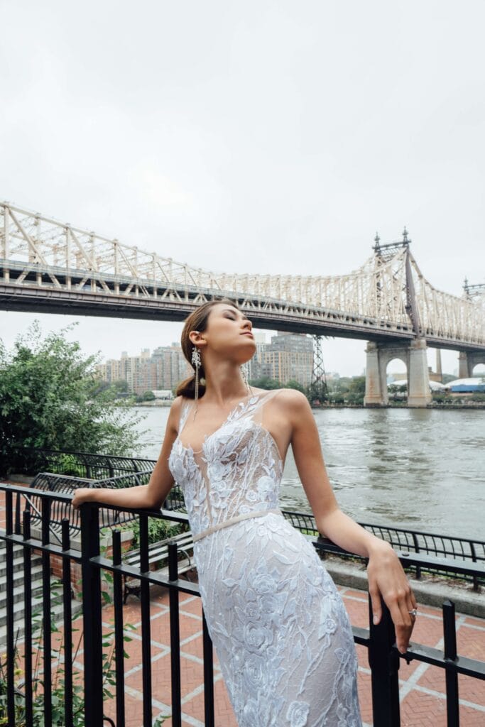 Woman in lace dress by river and bridge.