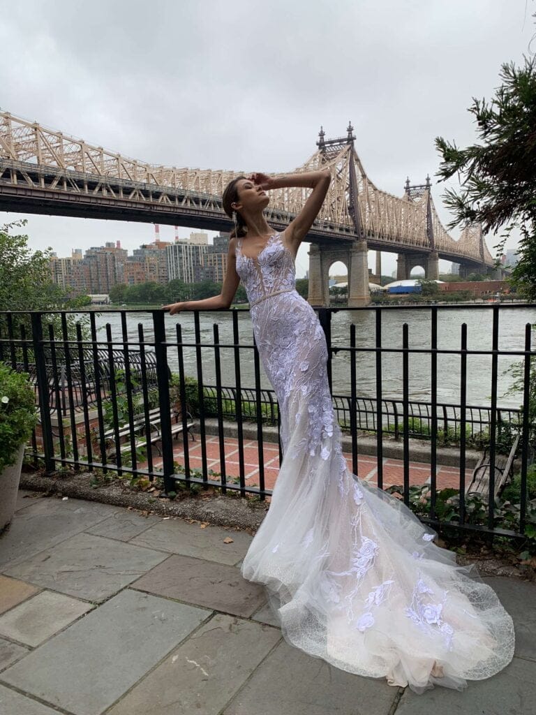 Bride poses by city bridge on cloudy day.
