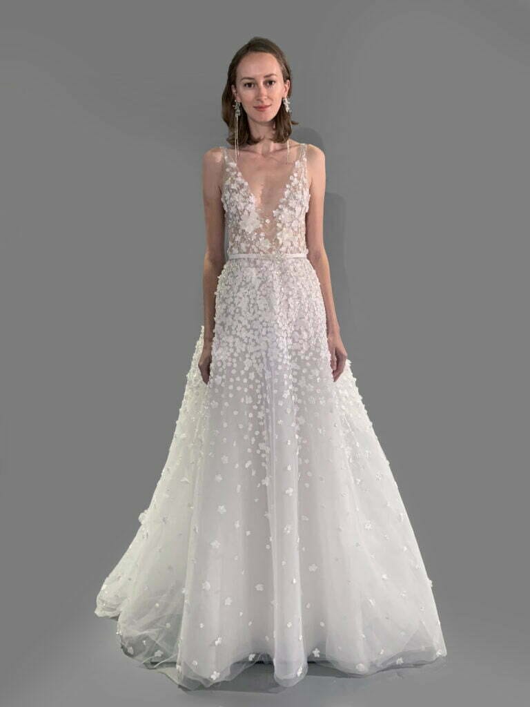 Woman in white floral gown against gray background.