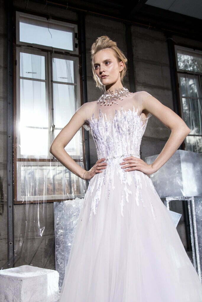 Woman in white embellished gown, hands on hips.