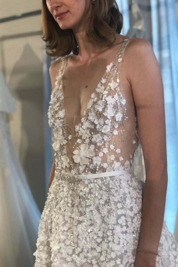 Woman in sheer floral embroidered wedding dress indoors.