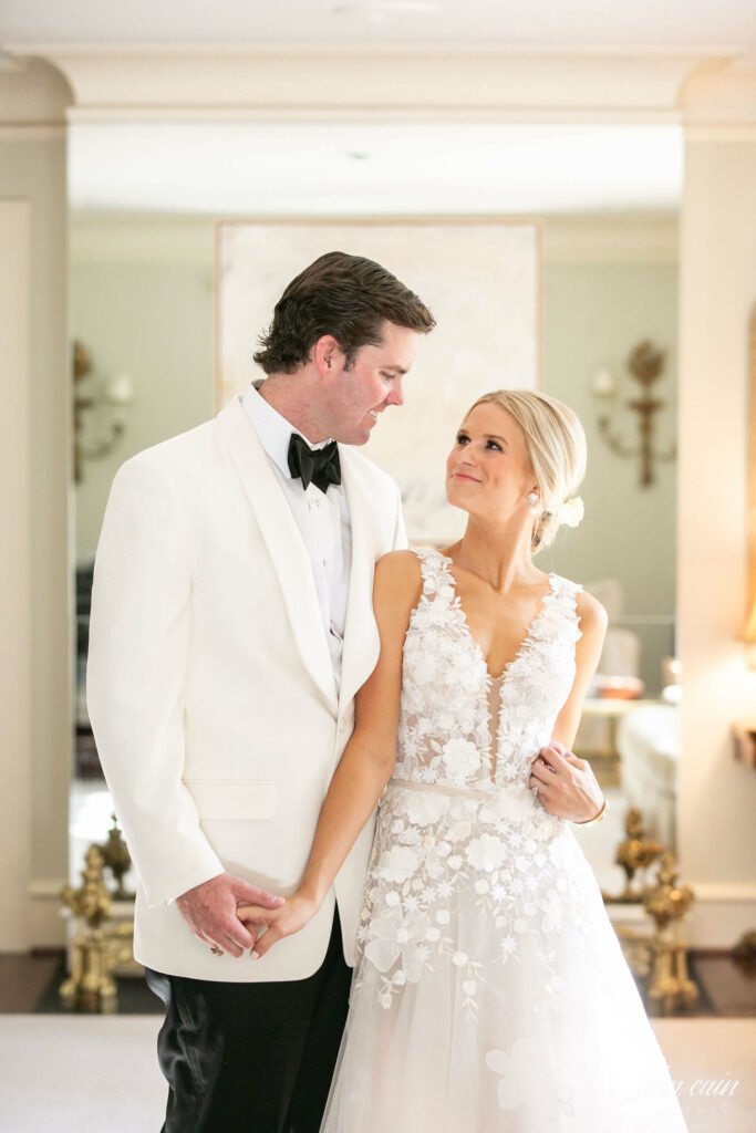Bride and groom smiling, holding hands indoors.