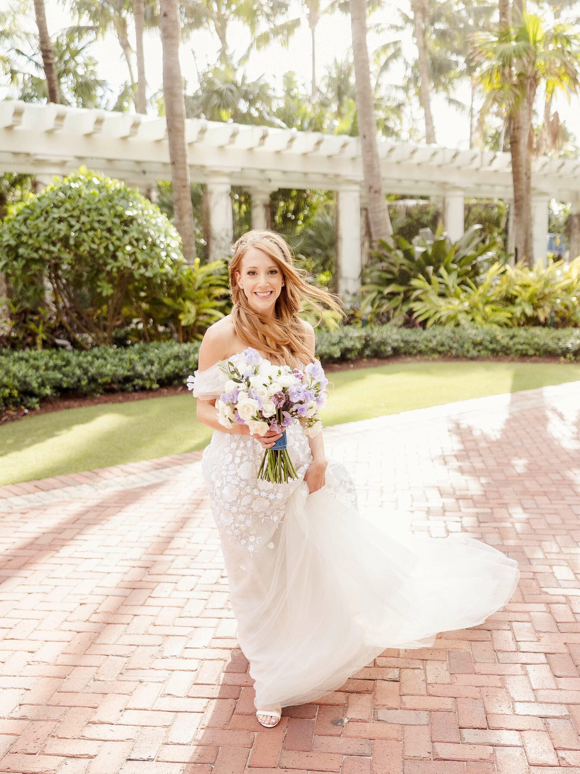 Smiling bride with bouquet on sunny path.