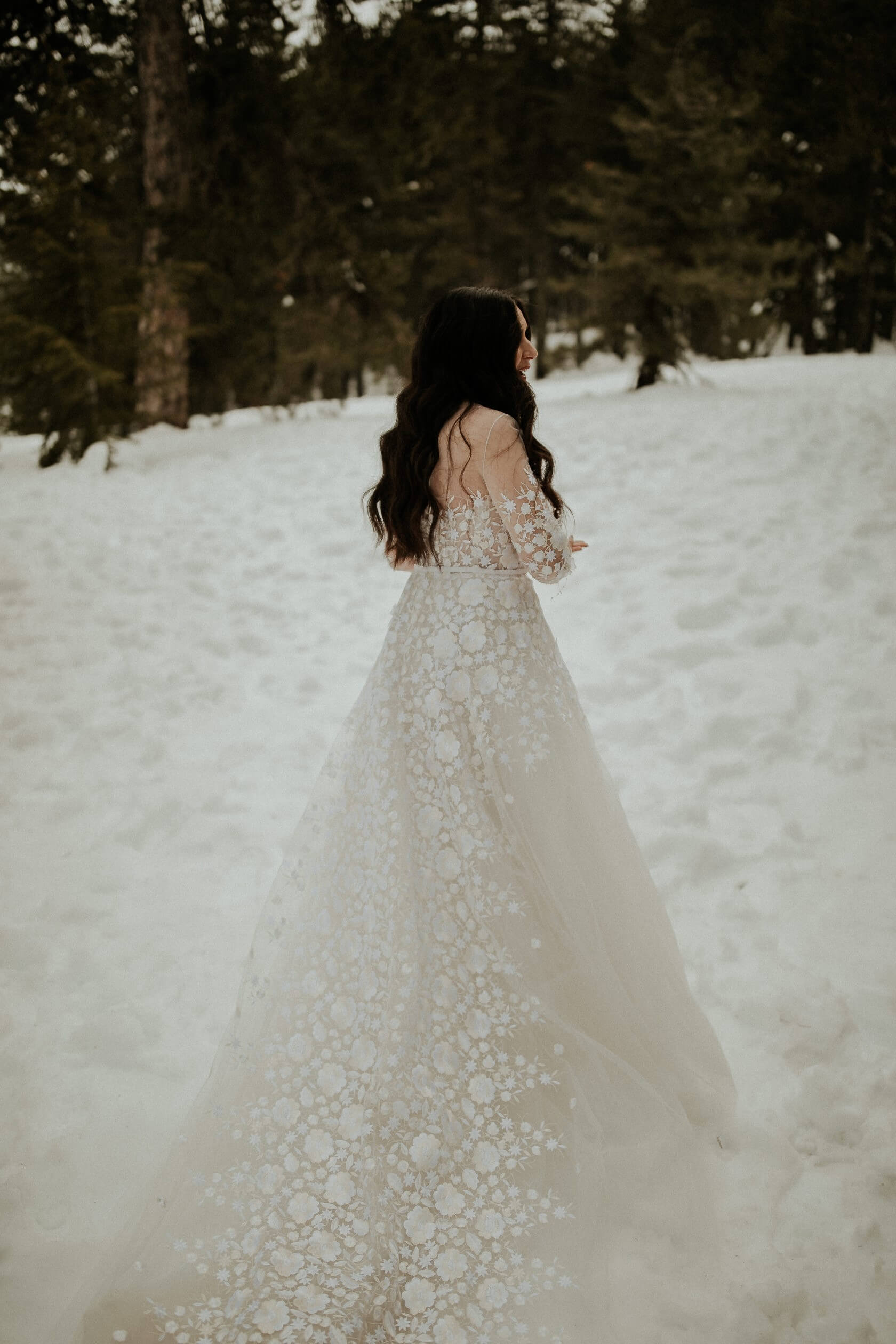Bride in lace dress walks in snowy forest.