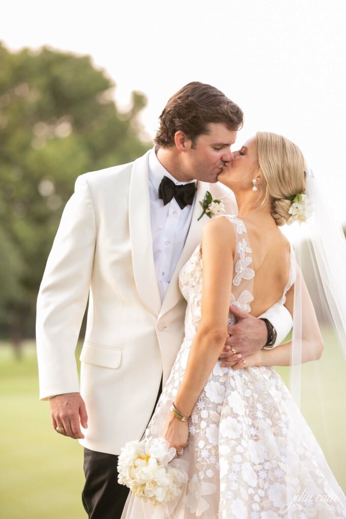Bride and groom kiss outdoors, looking joyful.