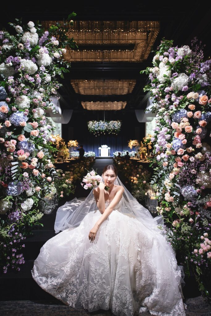 Smiling bride with bouquet amid floral arrangements.