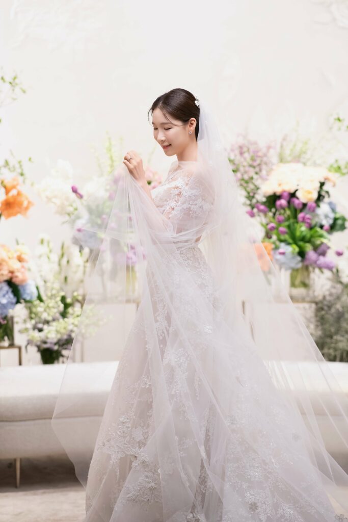 Smiling bride in lace dress, holding veil.