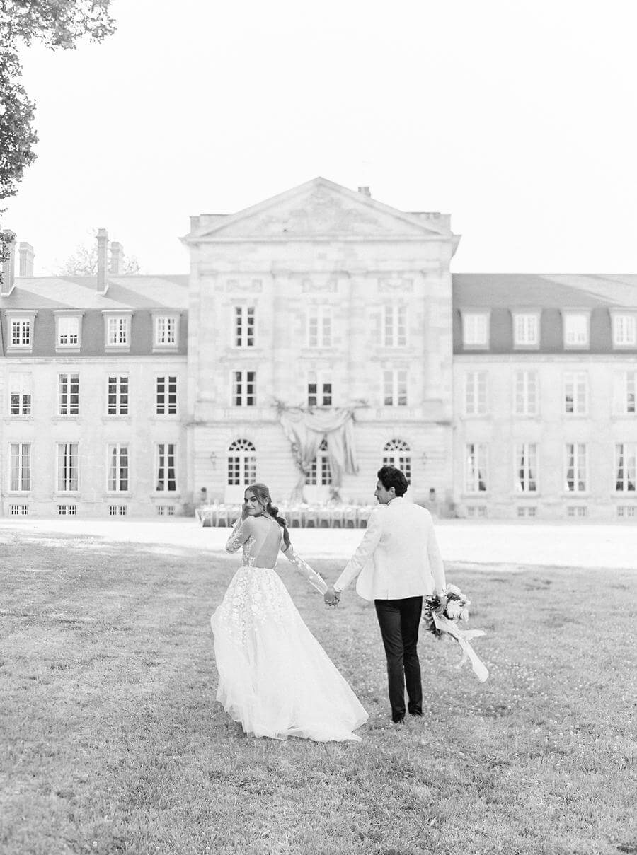 Bride and groom walk toward grand chateau.