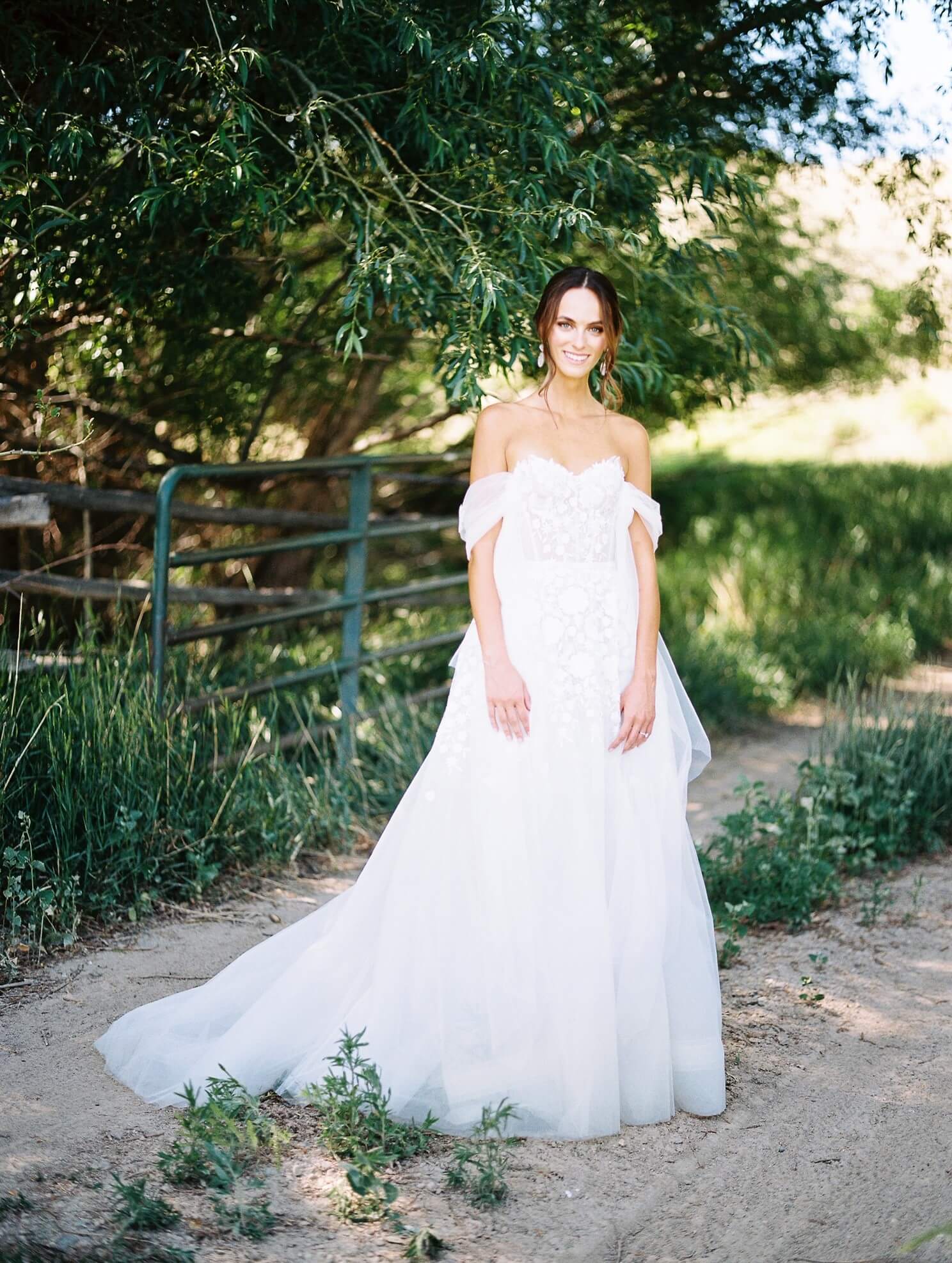Smiling bride outdoors in sunlight near trees.