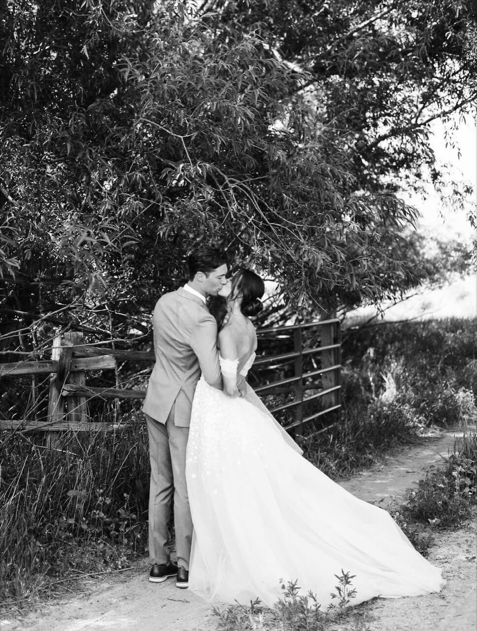 Bride and groom embrace on path, black-and-white.
