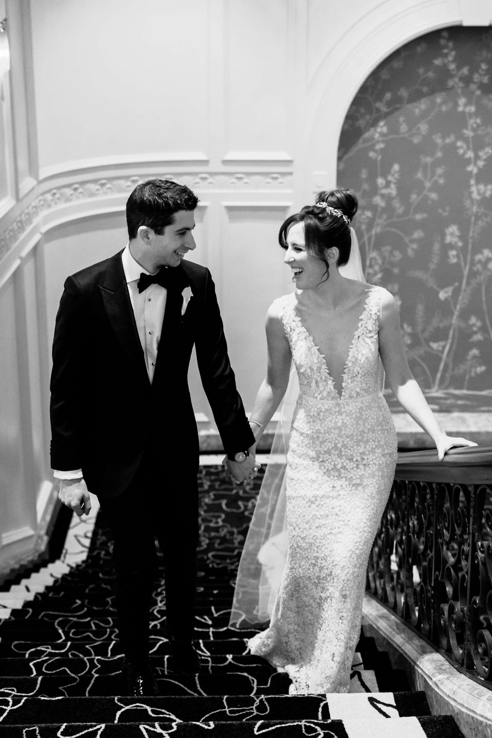 Bride and groom hold hands on ornate stairs.
