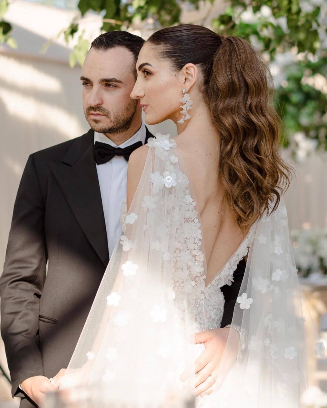 Bride and groom posing outdoors in sunlight.