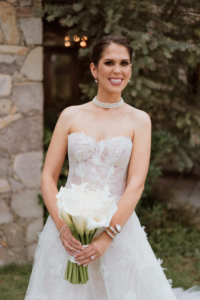 Bride in white gown holding calla lilies.