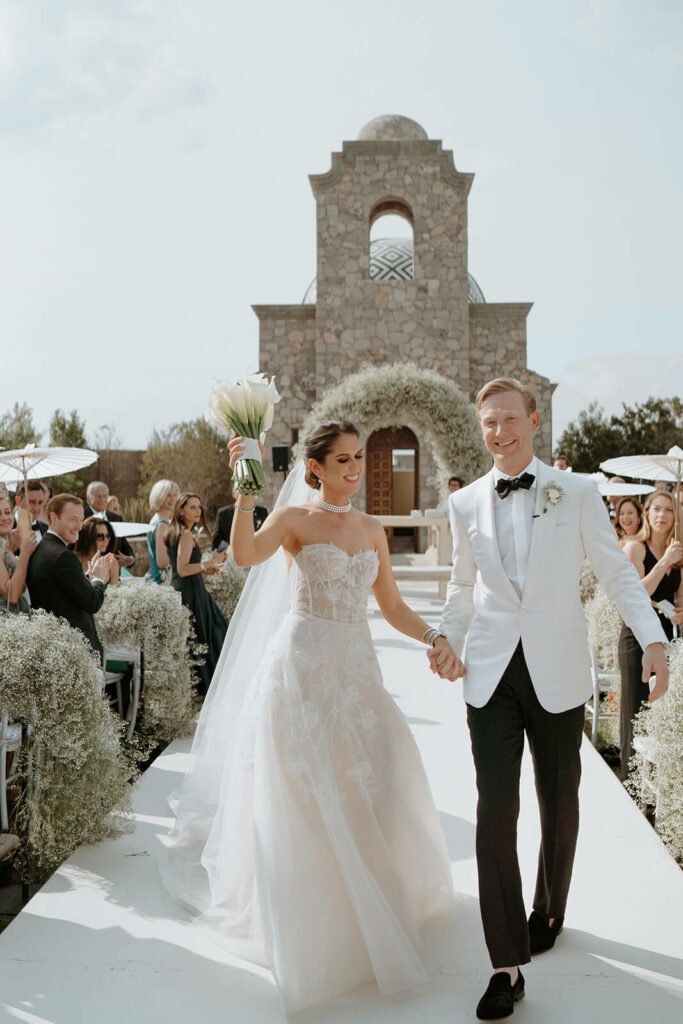 Smiling couple exits chapel amid clapping guests.