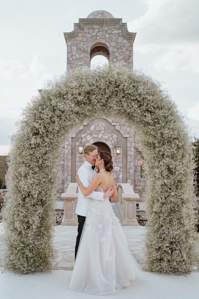 Bride and groom embrace under floral arch.