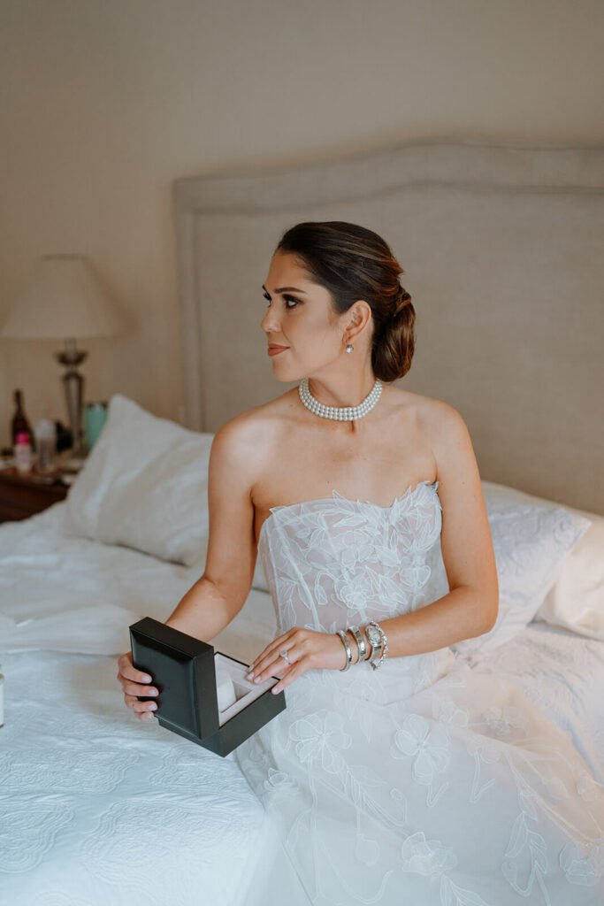Bride in white dress holds open jewelry box.