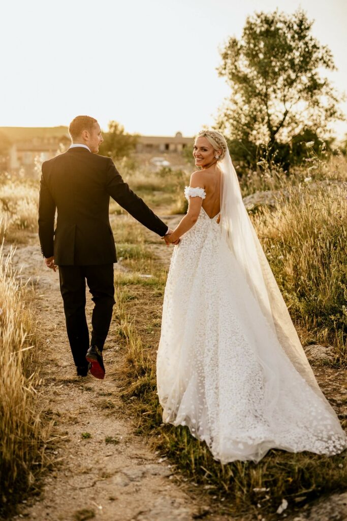Bride and groom walk outdoors, holding hands.