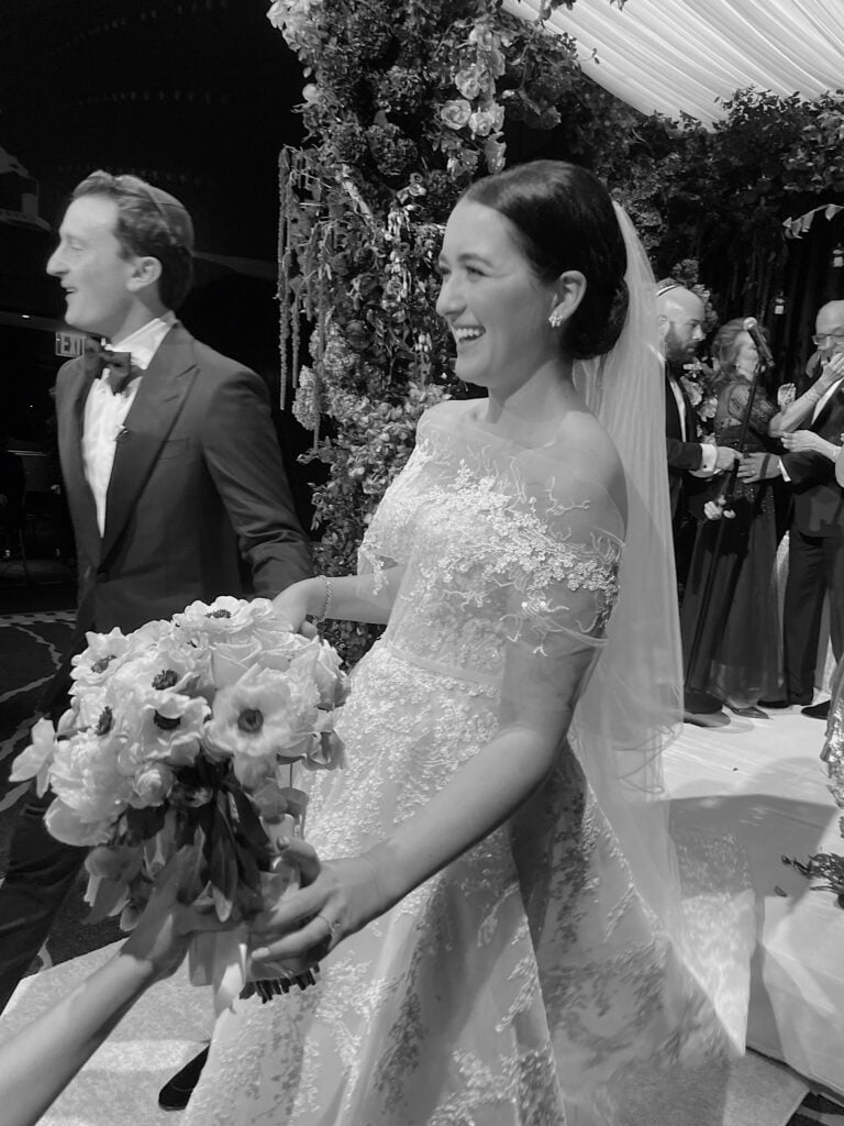 Smiling bride and groom walk amid flowers.