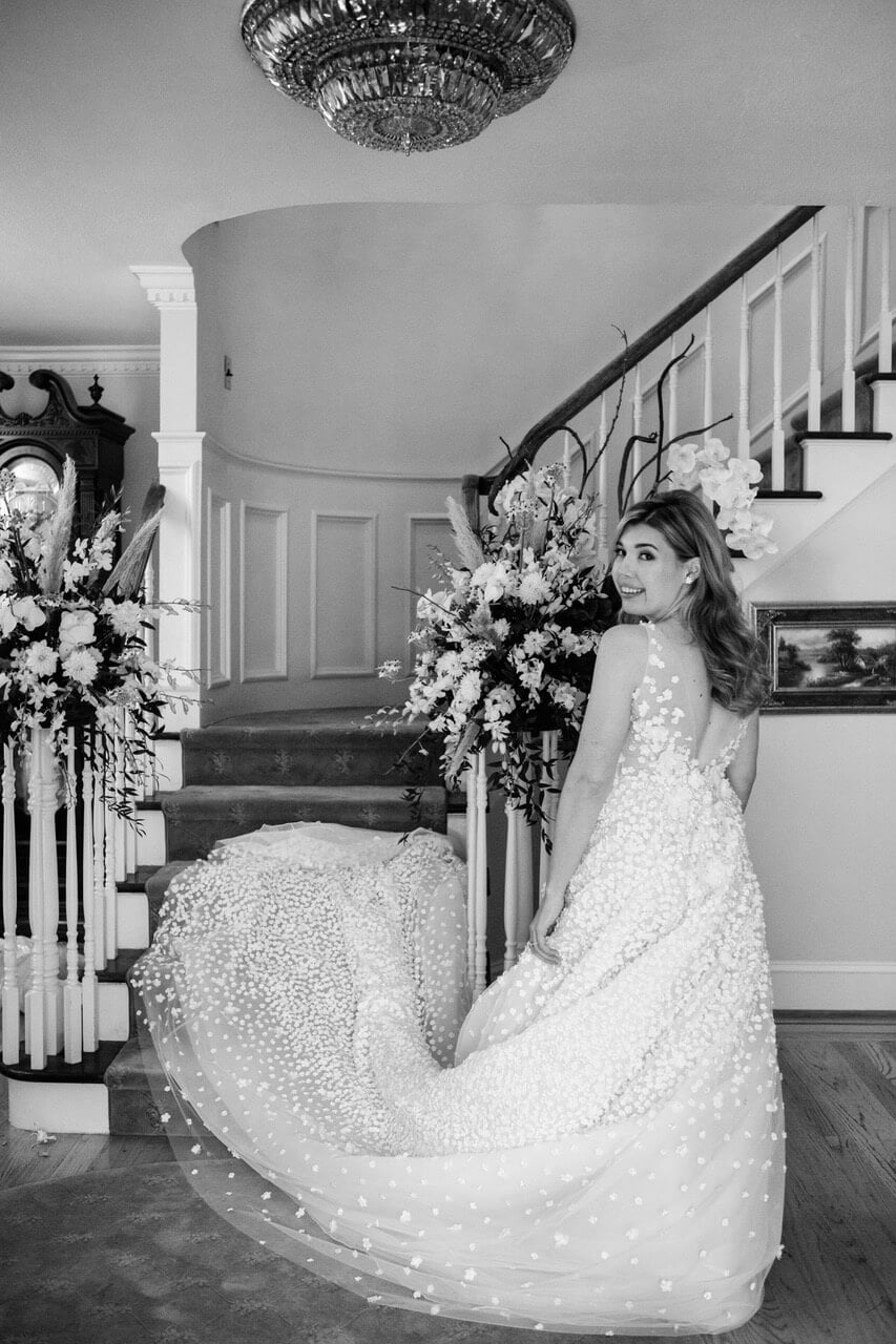 Bride in floral gown by decorated staircase.