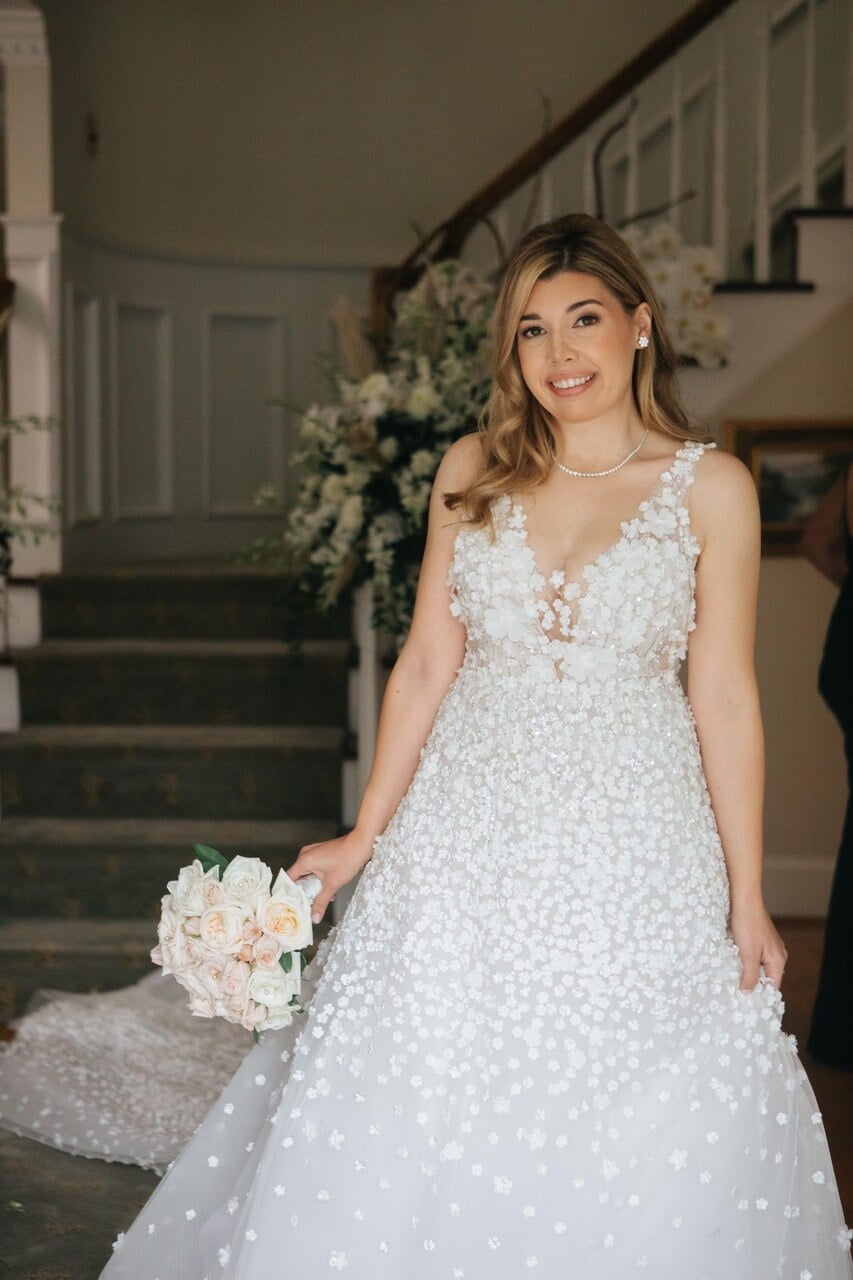Smiling bride with bouquet by floral staircase.
