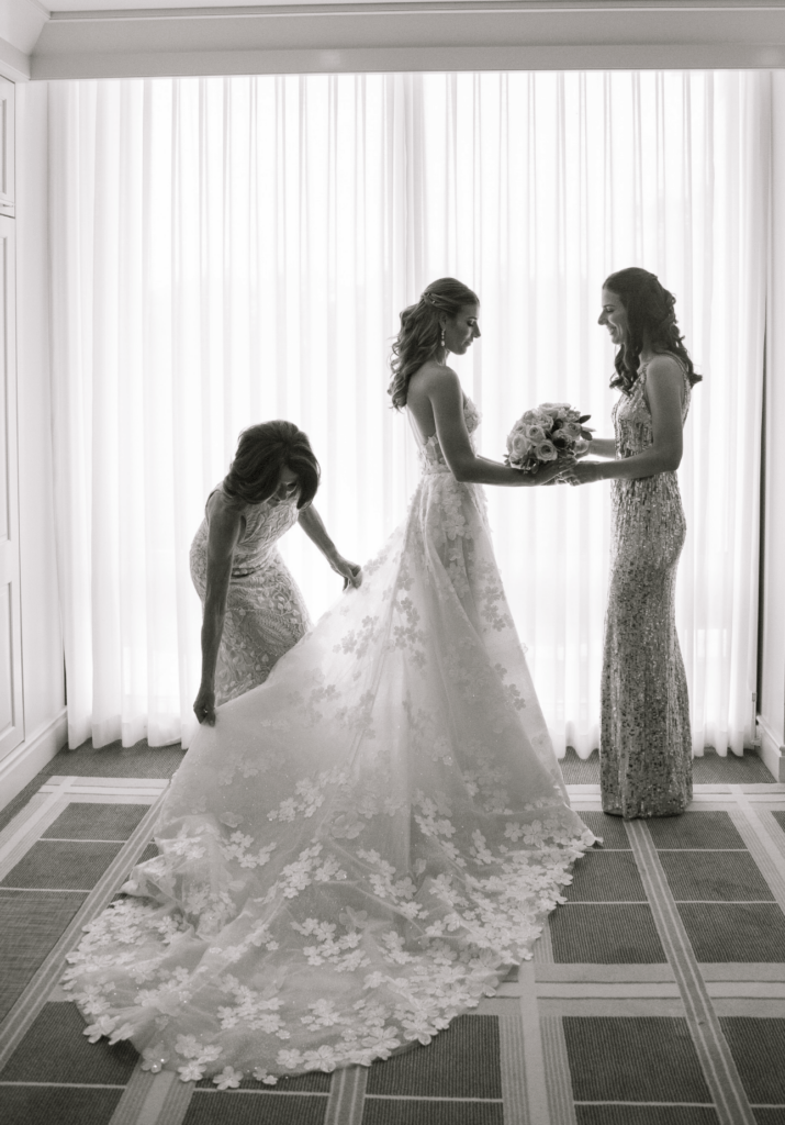 Bride with bridesmaids; dress adjusted, bouquet held.