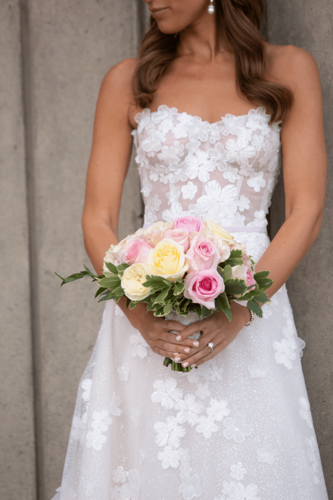 Bride in lace dress holding rose bouquet.