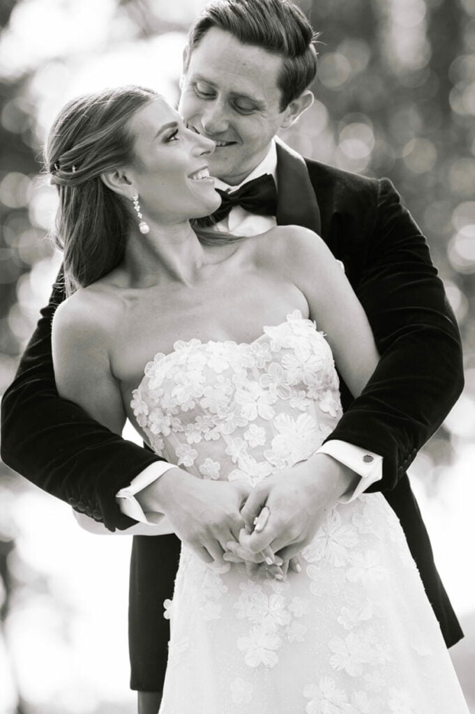 Bride and groom smiling, embracing outdoors, black-and-white.