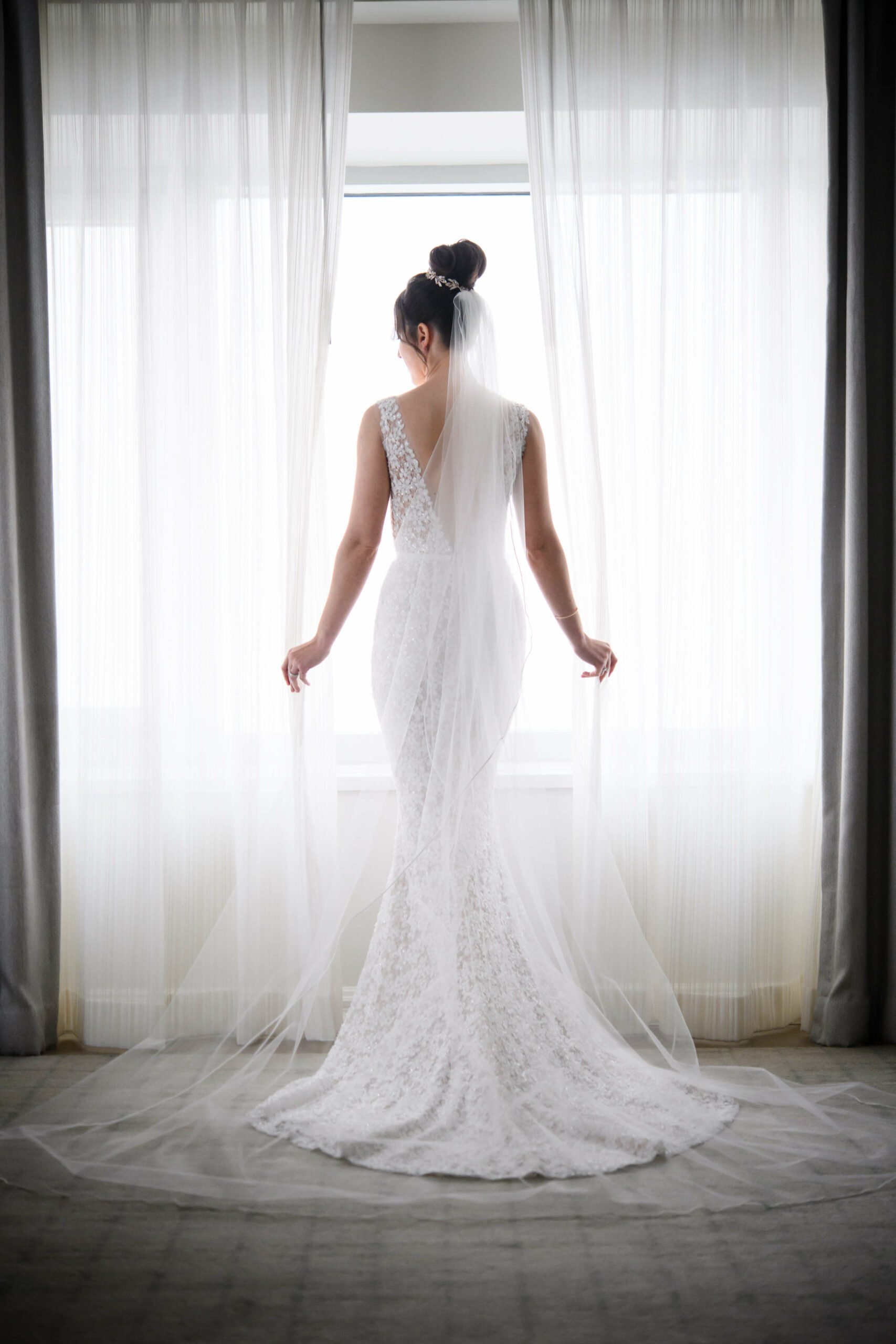 Bride in lace gown by sunlit window.