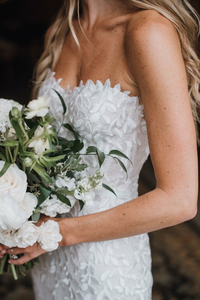 Bride holding bouquet, wearing lace wedding dress.