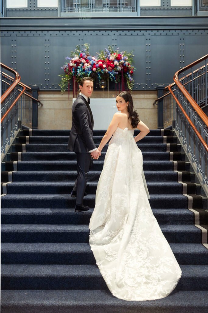 Bride and groom hold hands on staircase.