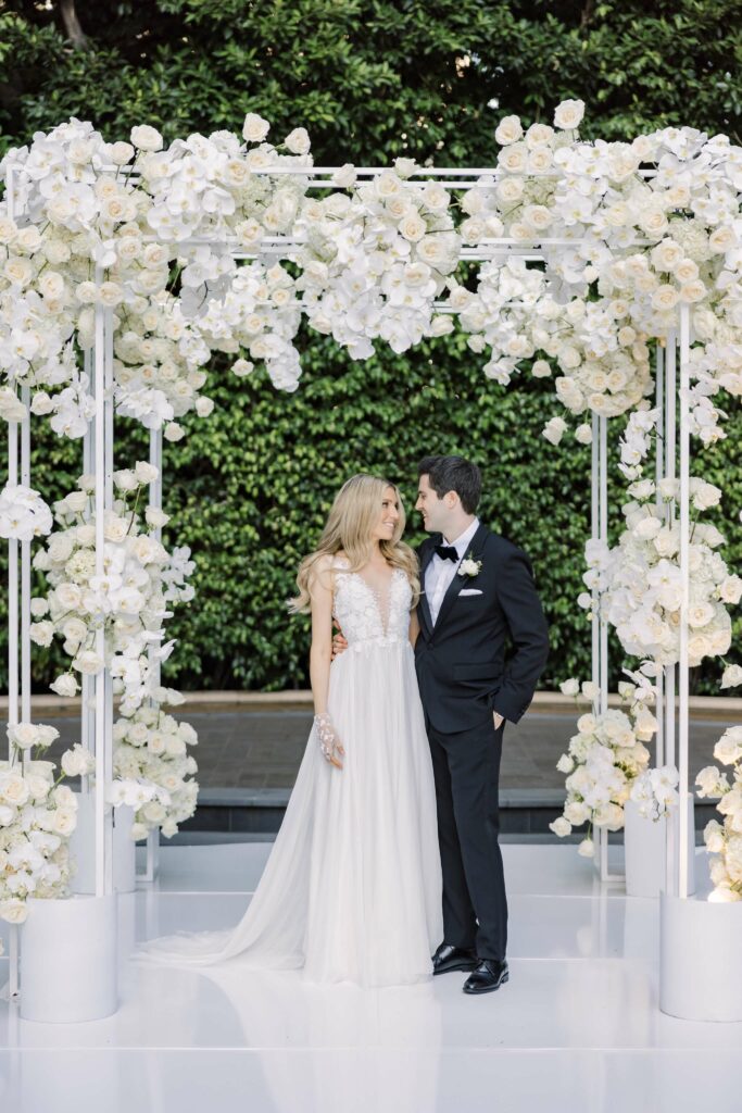 Bride and groom under floral arch outdoors.