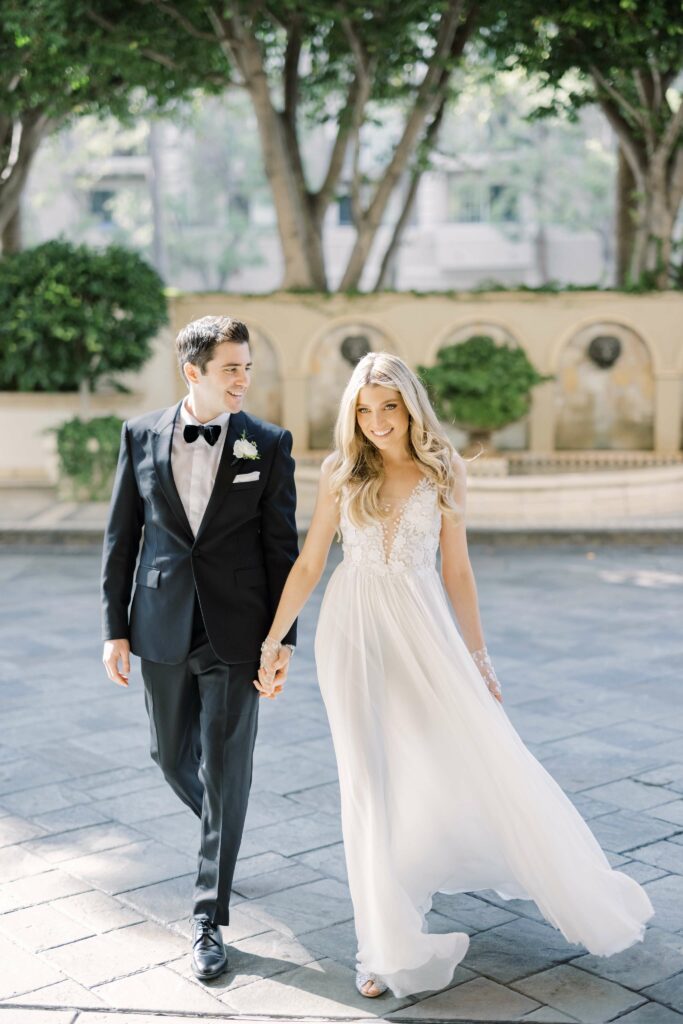 Bride and groom walk hand-in-hand outdoors.