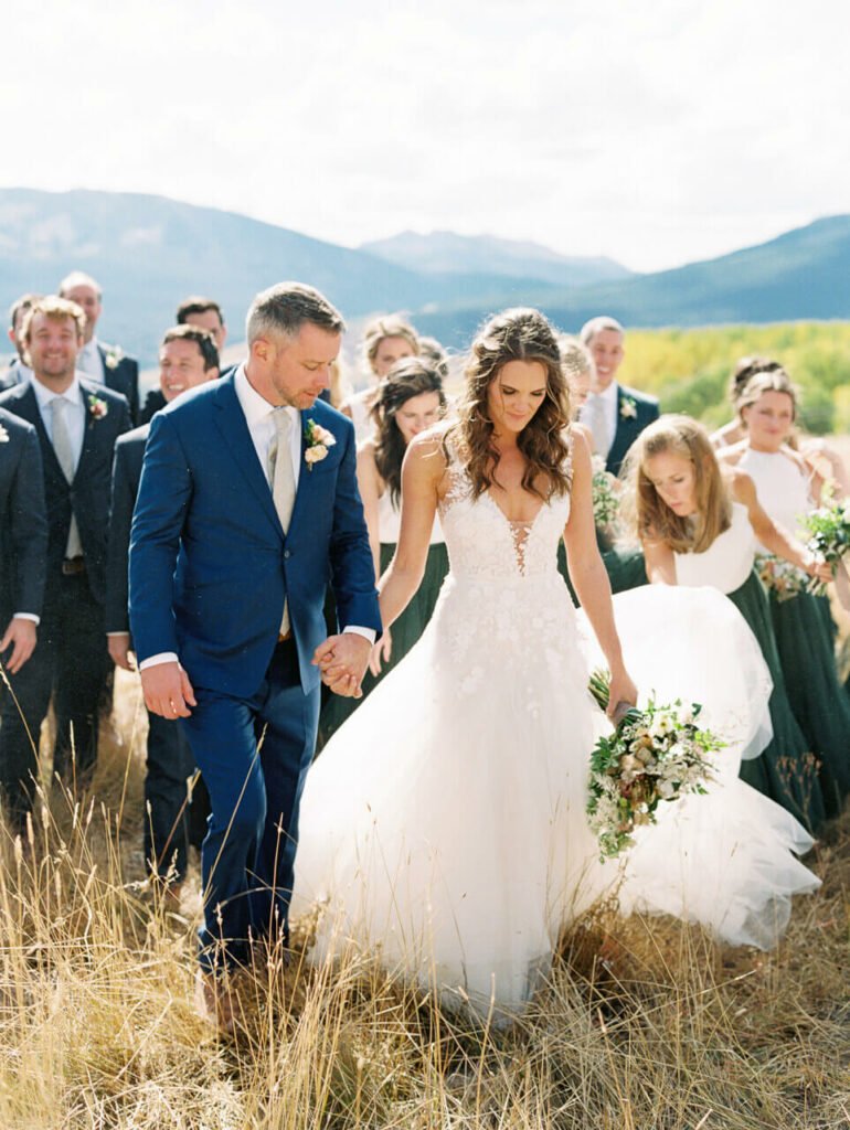 Bride and groom walk with wedding party outdoors.