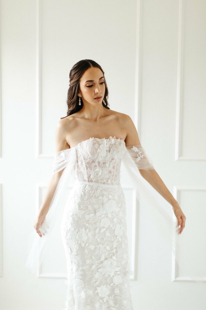 Bride in lace dress stands, looking down.