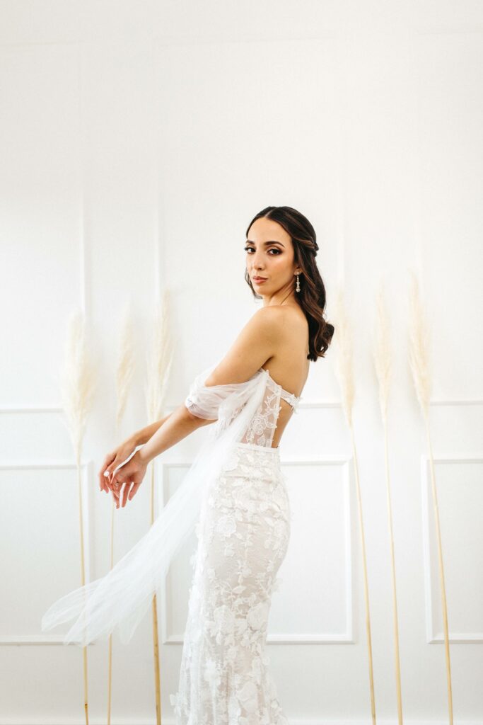 Bride in lace gown poses by pampas grass.