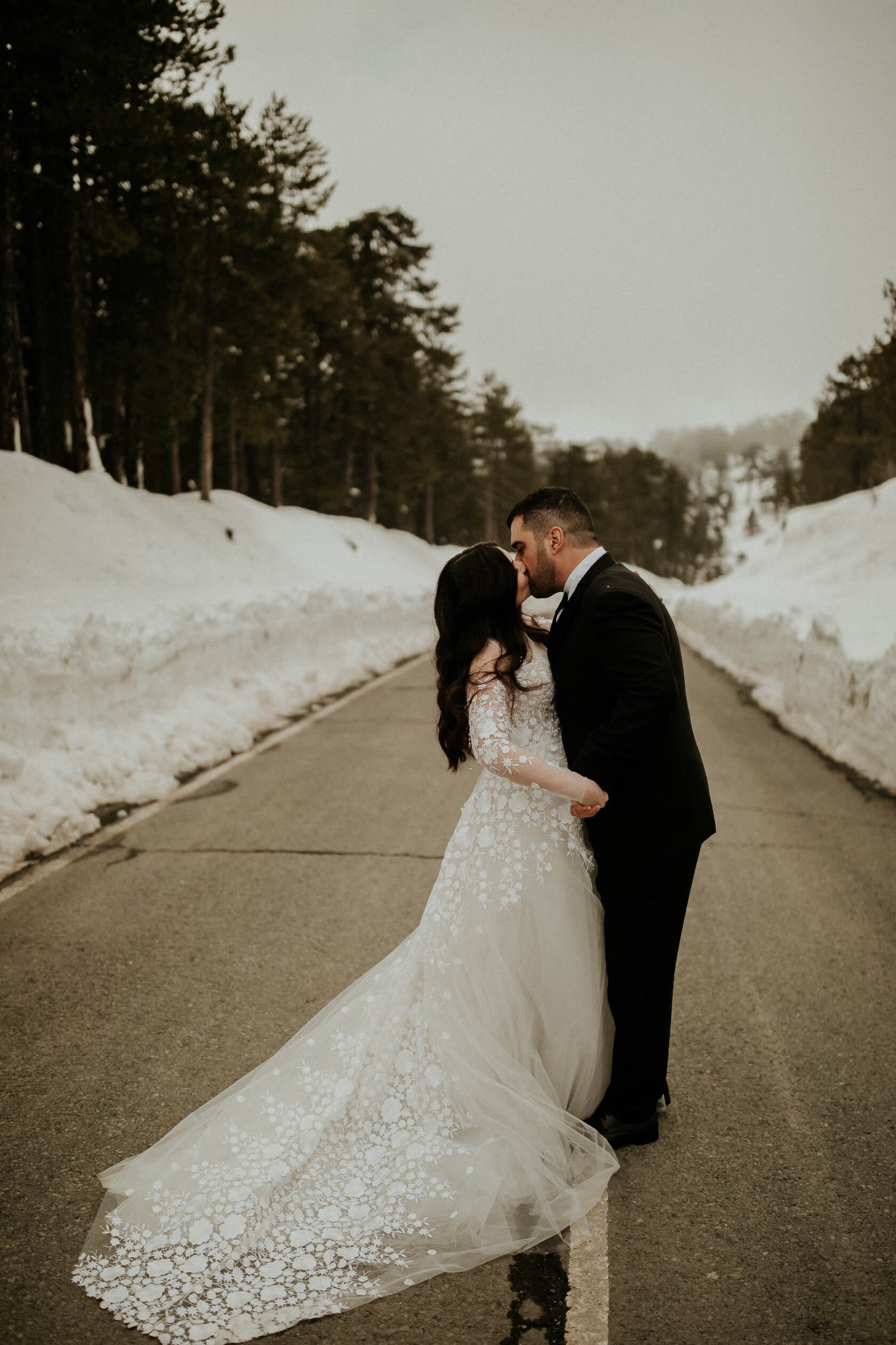 Bride and groom kiss on snowy road.