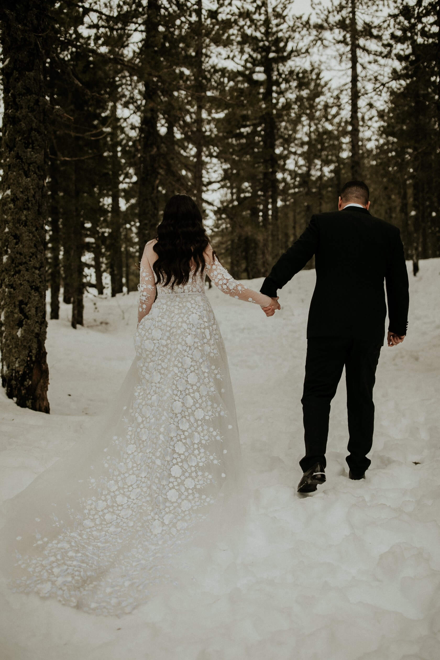 Bride and groom walk hand-in-hand in snow.