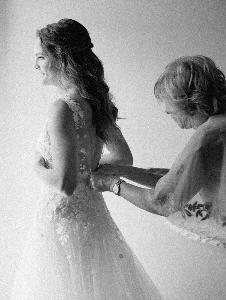 Bride smiling as older woman buttons dress.