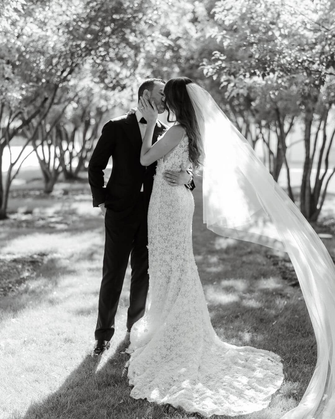 Bride and groom kiss outdoors under sunlight.