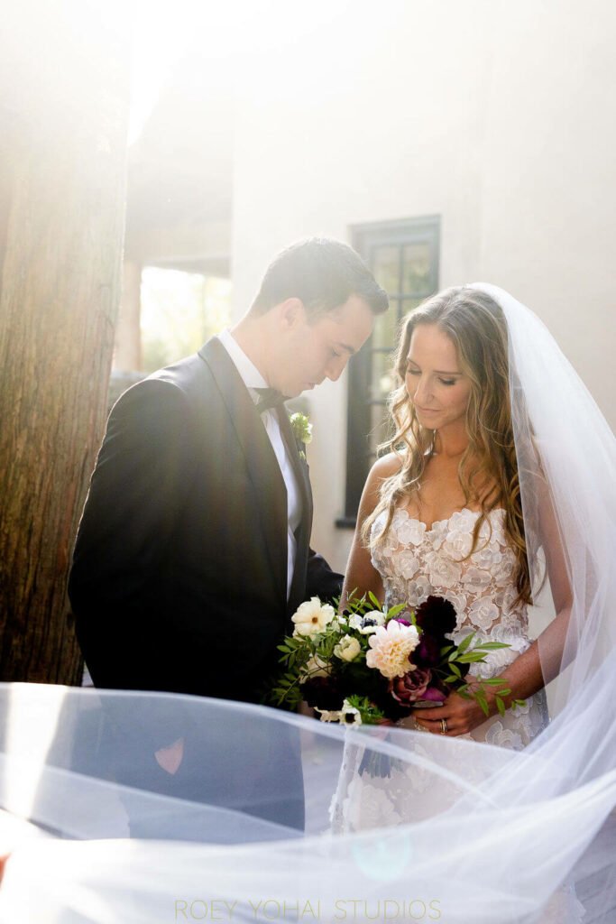 Bride and groom embracing outdoors with bouquet.