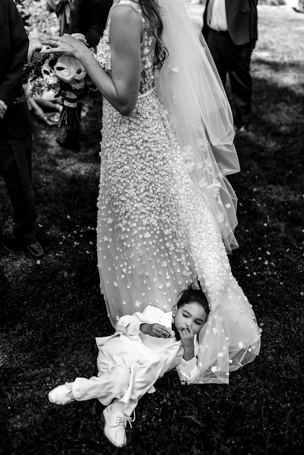 Child sleeps on brides dress outdoors, grayscale.