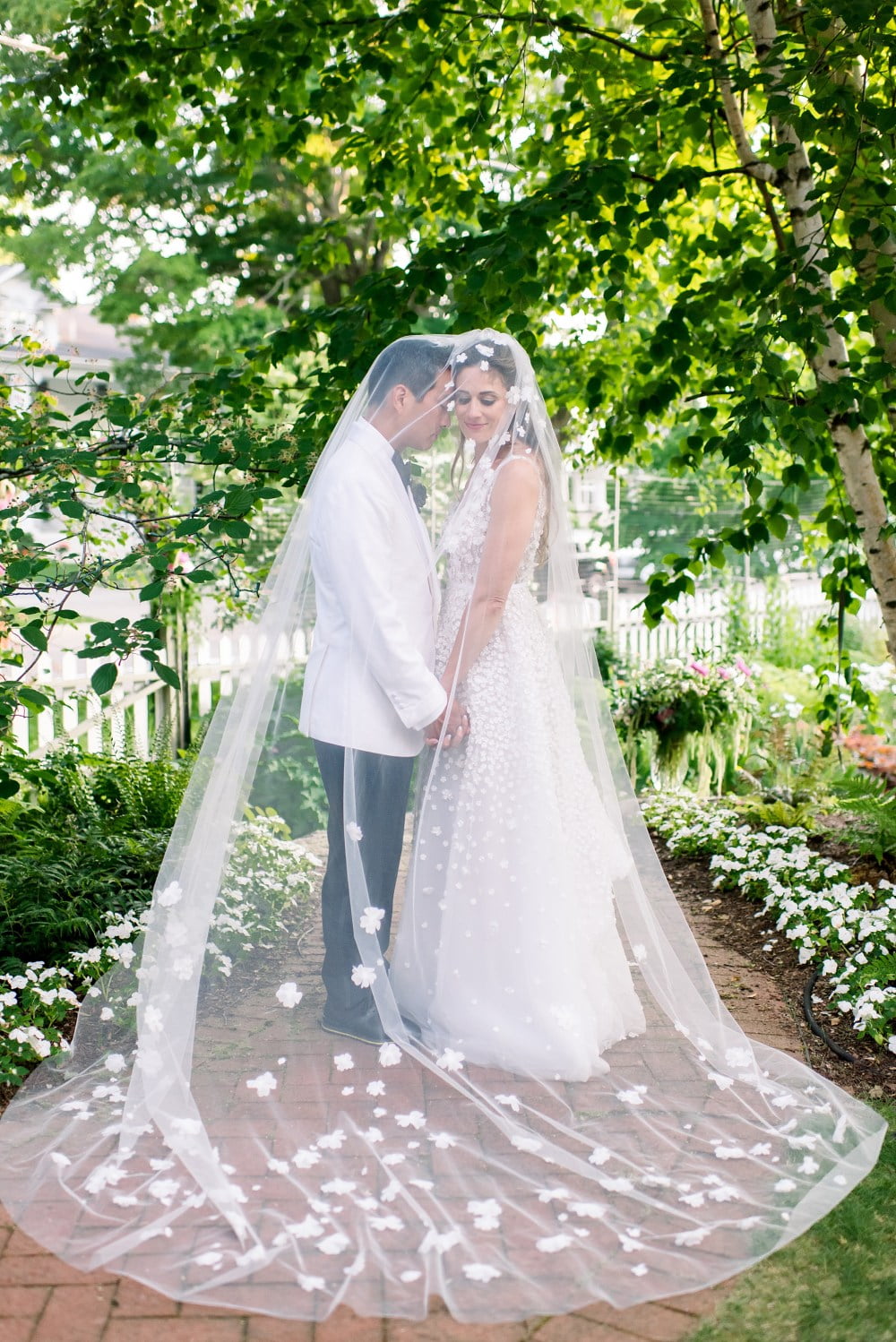 Bride and groom smiling under sheer veil outdoors.
