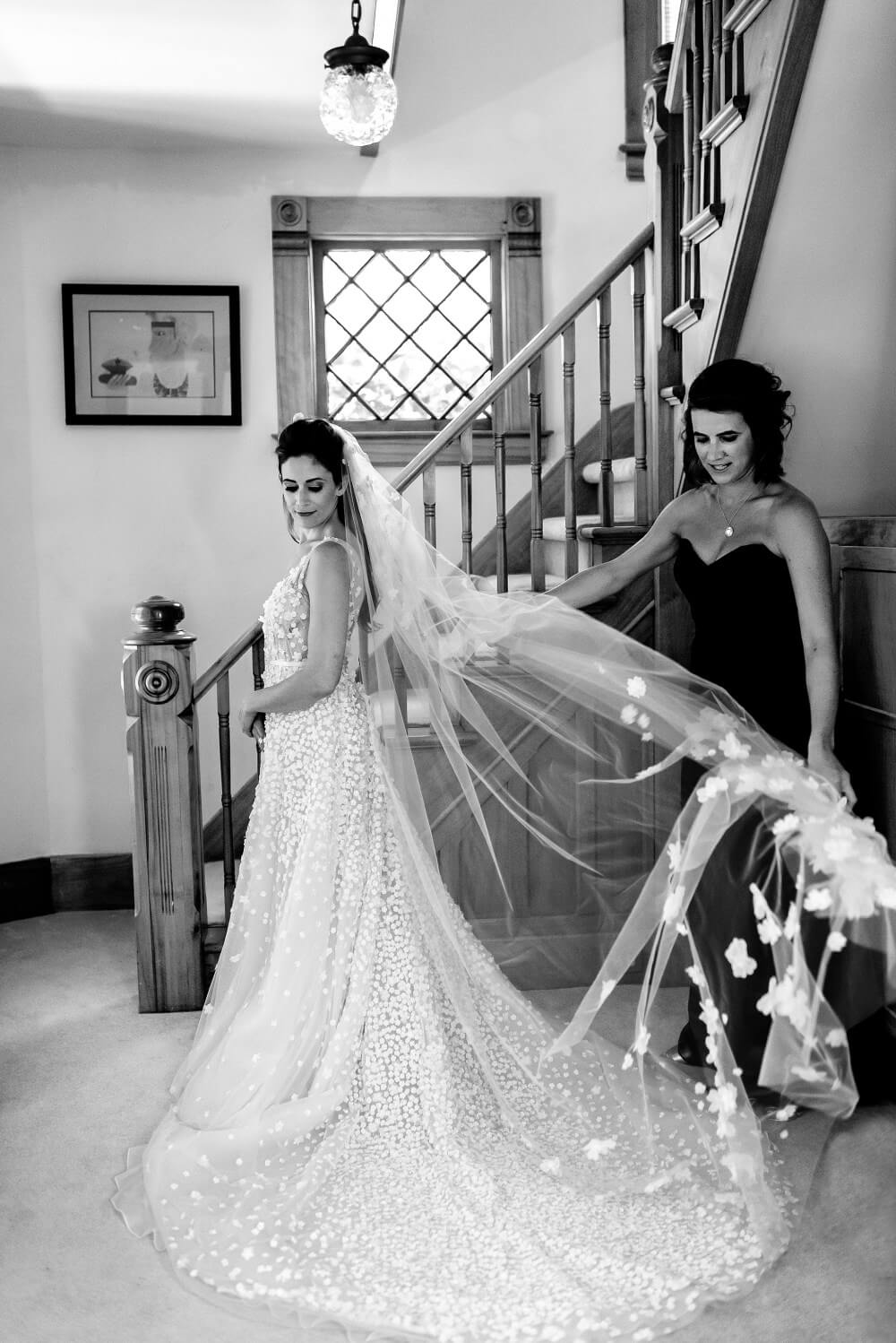 Bride at staircase, woman holds her veil.